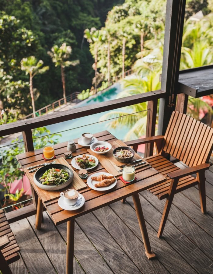 Table with served breakfast on wooden terrace with pool and jungle view in Bali